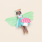 Colorful fairy toy with green wings and a polka dot mushroom on a beige background