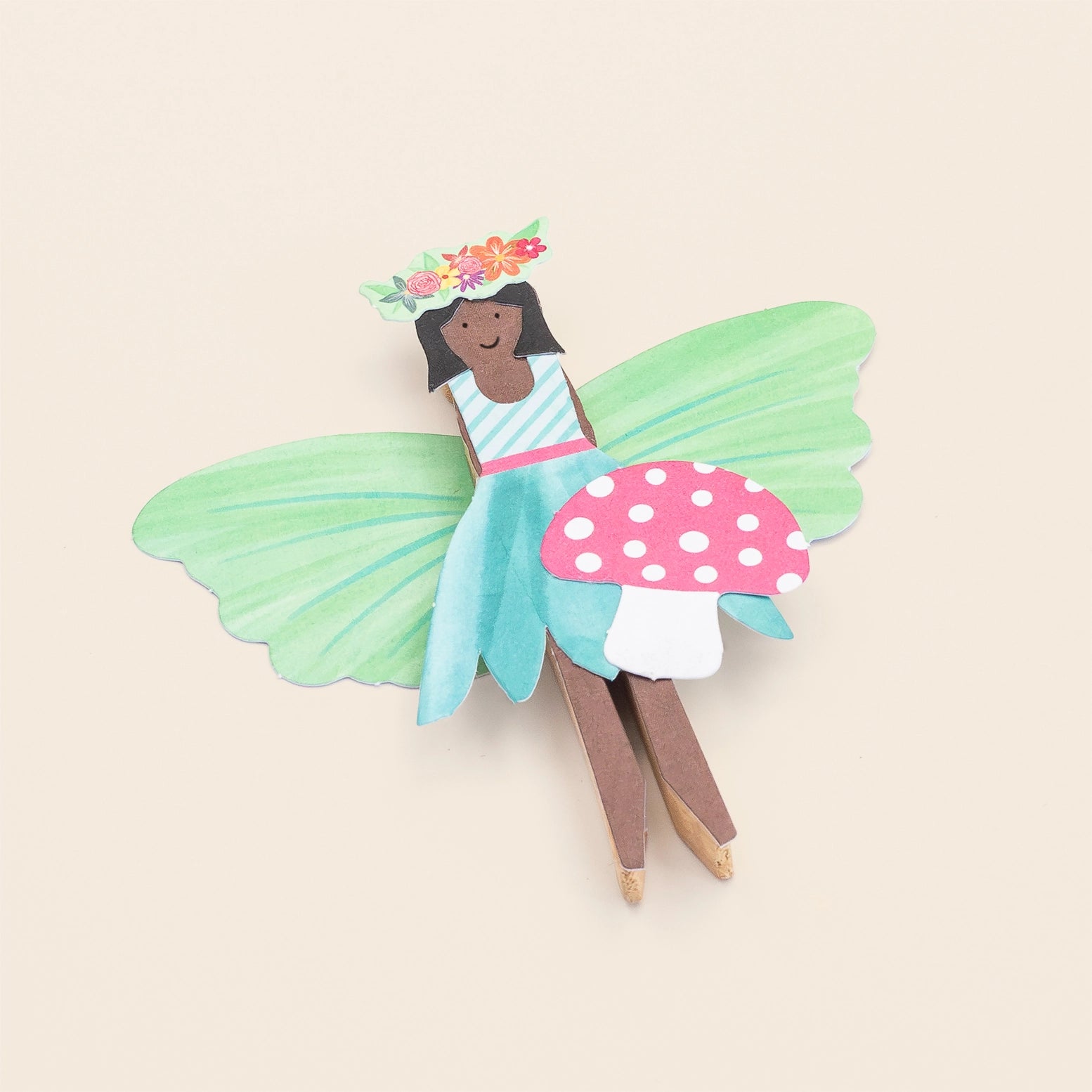 Colorful fairy toy with green wings and a polka dot mushroom on a beige background