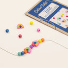 Colorful bead bracelet with rainbow shapes next to a craft kit on a beige background