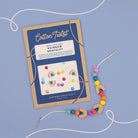 Cotton Twist craft kit for making a rainbow bracelet on a blue background