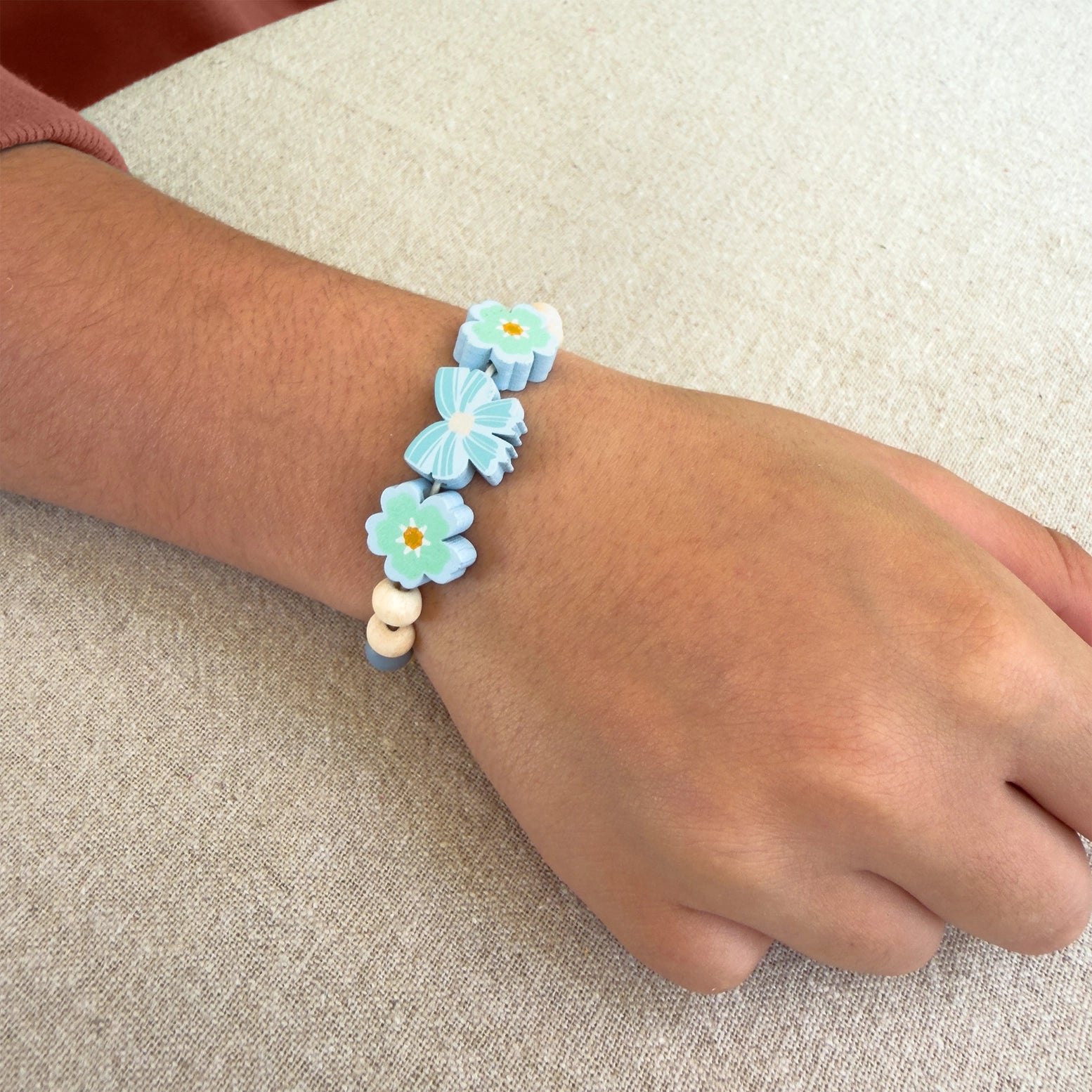 Child's wrist wearing a bracelet with blue flower-shaped beads on a beige fabric background
