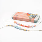 Colorful beaded jewelry making kit with a pink tin on a white background