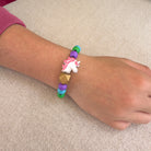 Colorful beaded bracelet with a unicorn charm on a wrist against a beige background