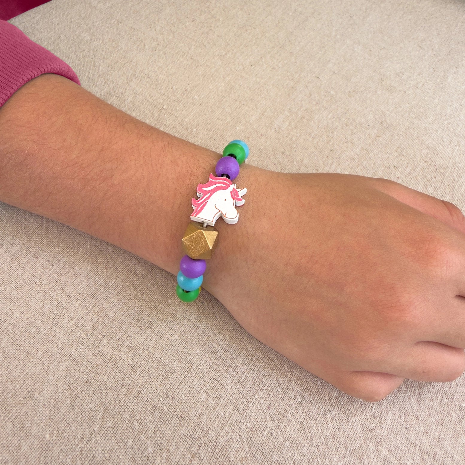 Colorful beaded bracelet with a unicorn charm on a wrist against a beige background