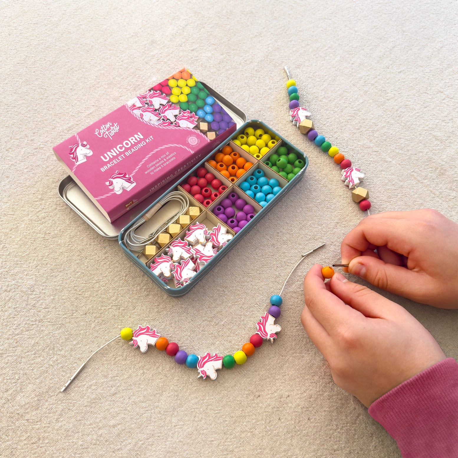 Colorful bead kit with unicorn-themed beads and a child's hands working on a beaded necklace.