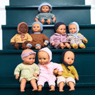 Set of Djeco Pomea baby dolls in various outfits sitting on a set of stairs.