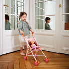 Child pushing a doll in a stroller in a room with large windows.