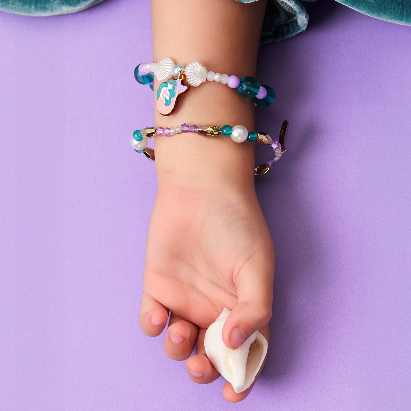 Child's hand wearing colorful mermaid bracelets on a purple background