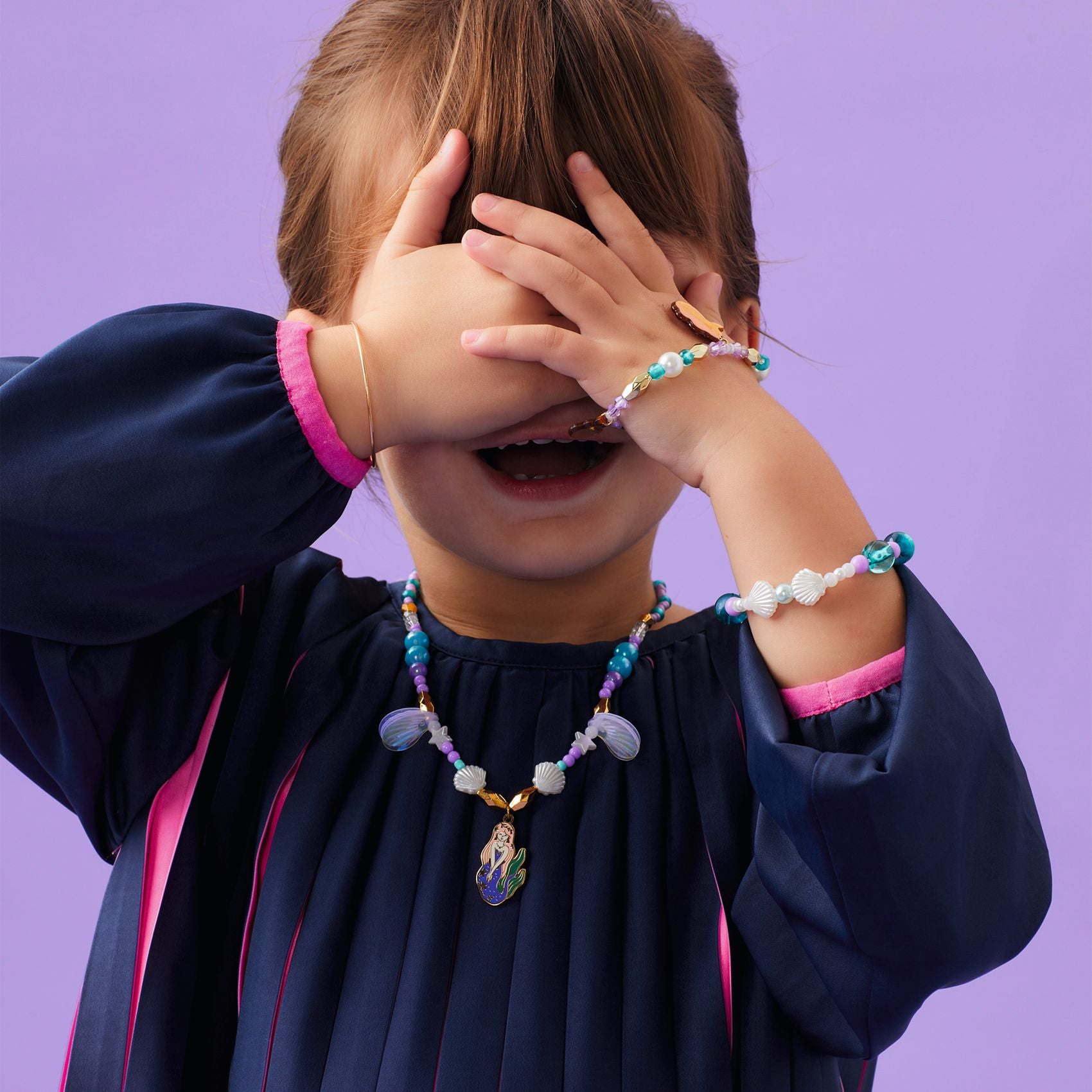 Child wearing colorful mermaid themed jewelry against a purple background