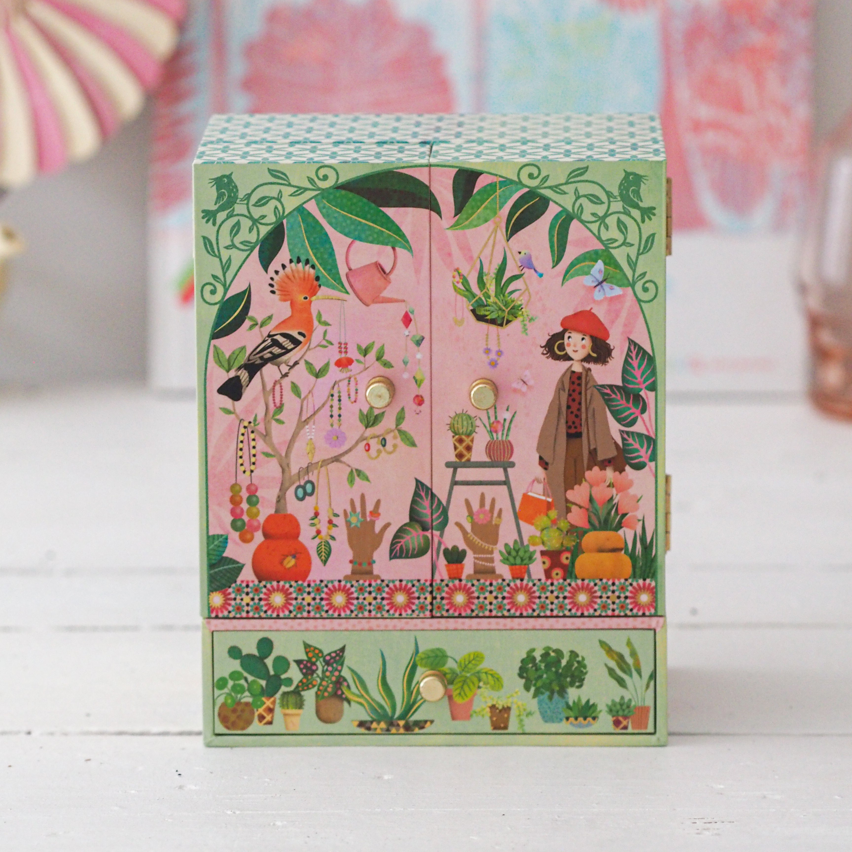 Decorative box with colorful illustrations of plants, birds, and a figure on a pink background.
