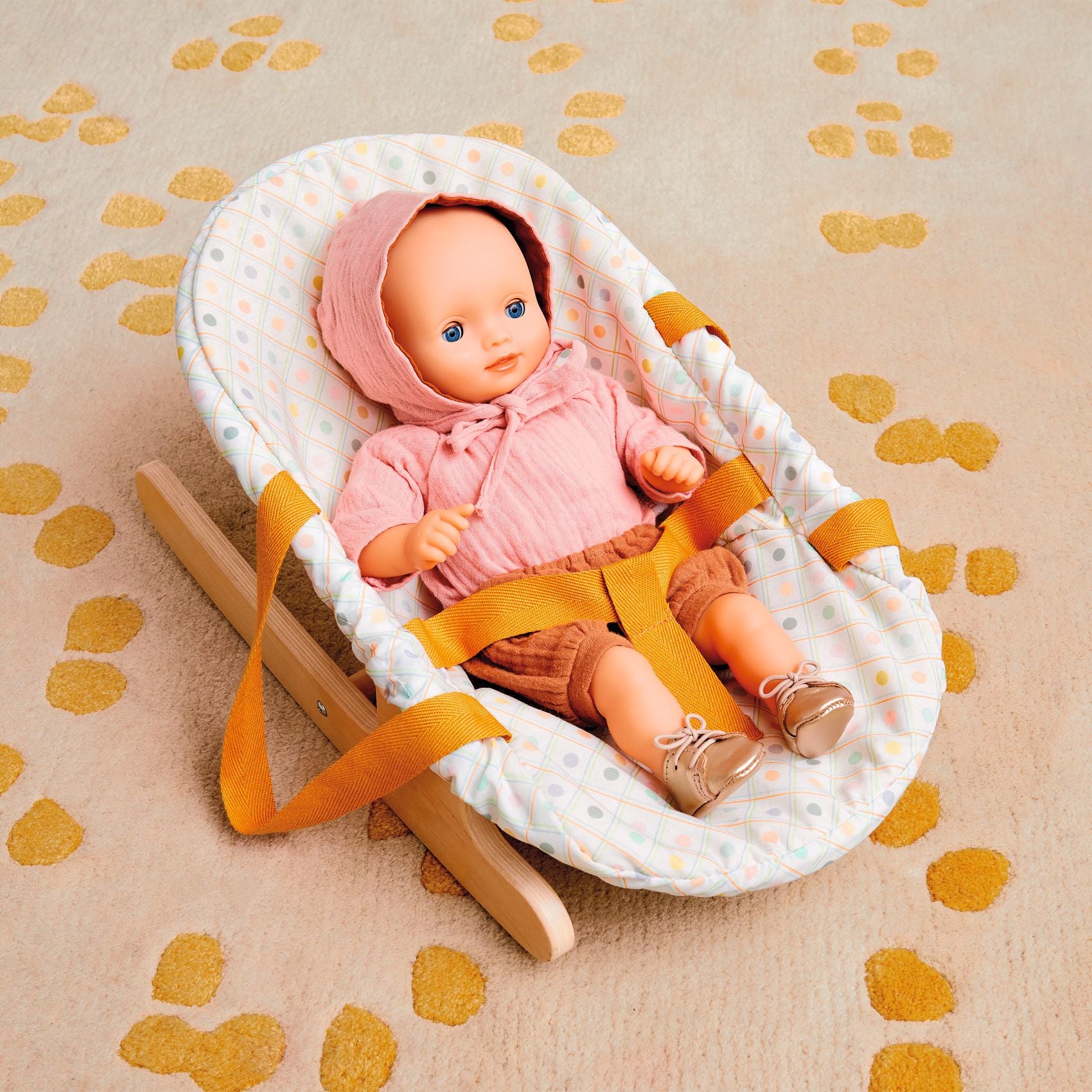 Baby doll in a white crib with orange straps on a beige surface with yellow footprints