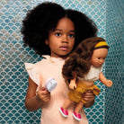 Young girl holding a doll and a brush against a patterned blue wall