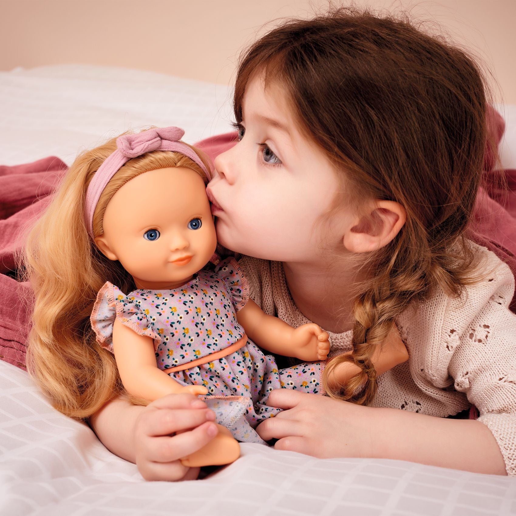 Child kissing a doll on the bed