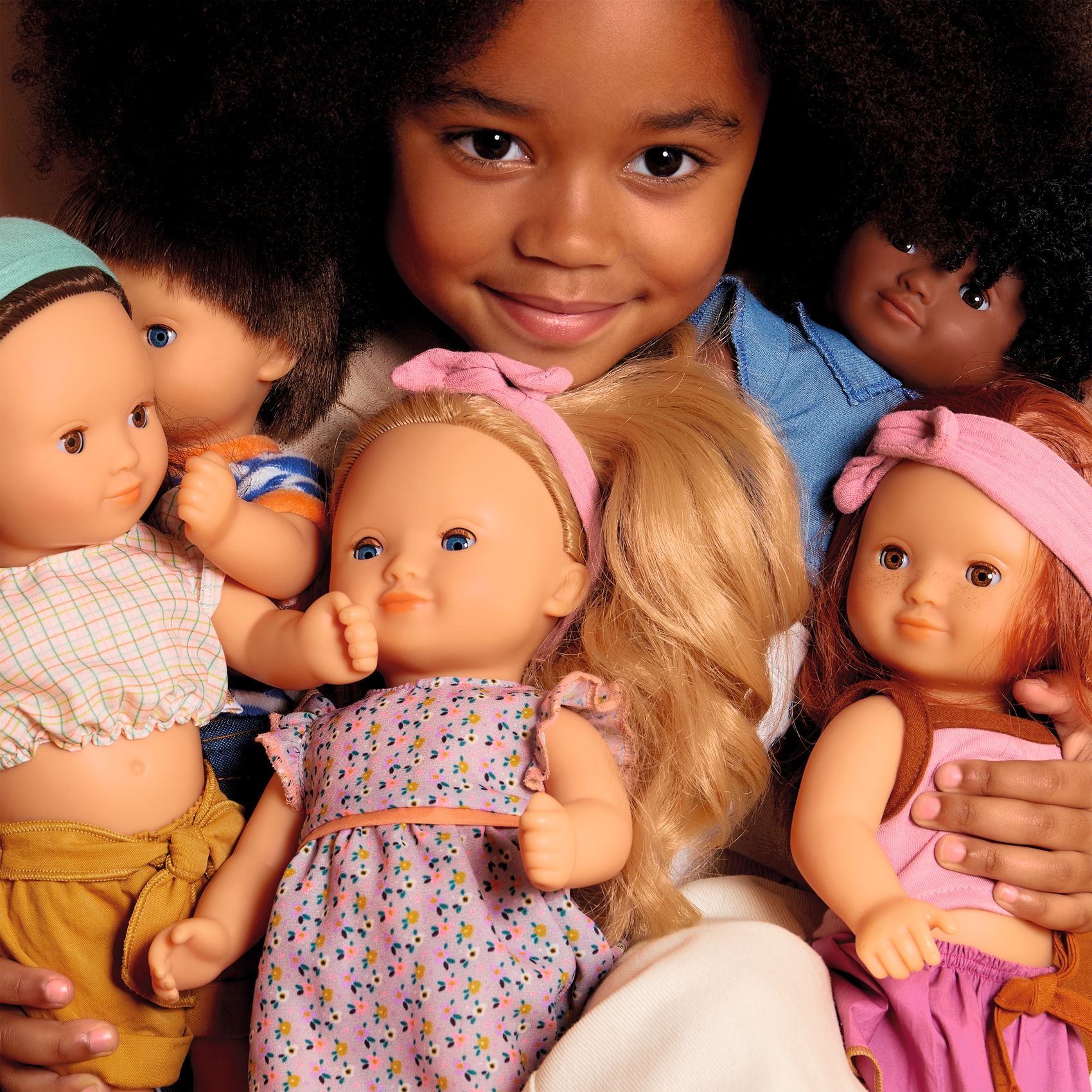 Child surrounded by a group of dolls with different hair colors and styles.