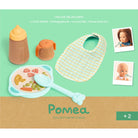 Pompea toy set with bib, bowl, spoon, and bottle on a green background