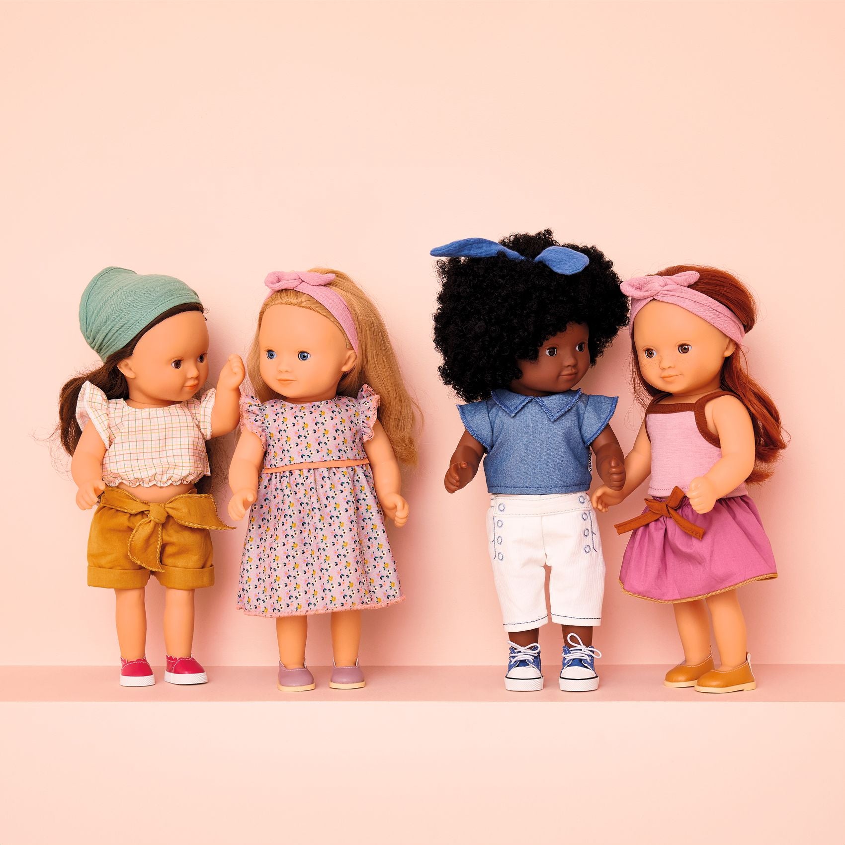Four dolls with different hairstyles and outfits on a pink background