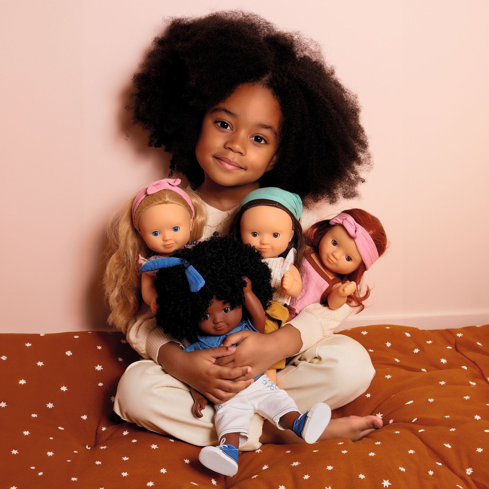 Child with four dolls on a bed with a pink background