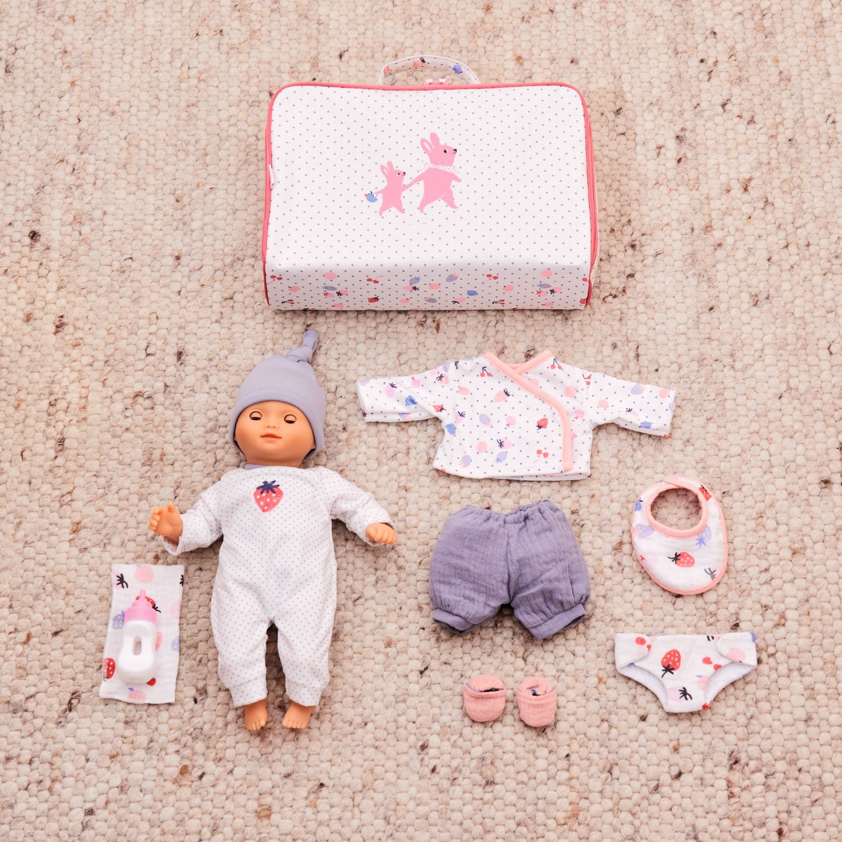 Baby doll with accessories including a suitcase on a beige carpet