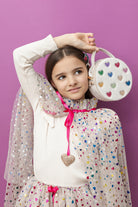 Young girl holding a heart-patterned handbag against a purple background