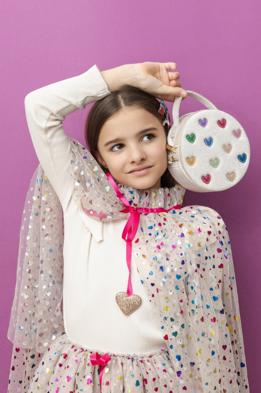 Young girl holding a heart-patterned handbag against a purple background