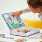 Child playing with a colorful puzzle book featuring a unicorn on a white surface.