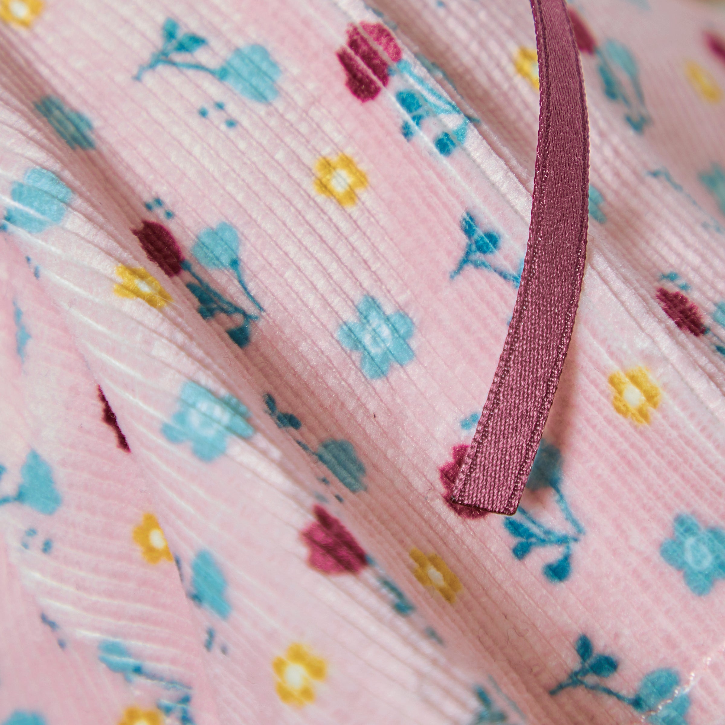 Close-up of pink fabric with floral pattern and purple ribbon
