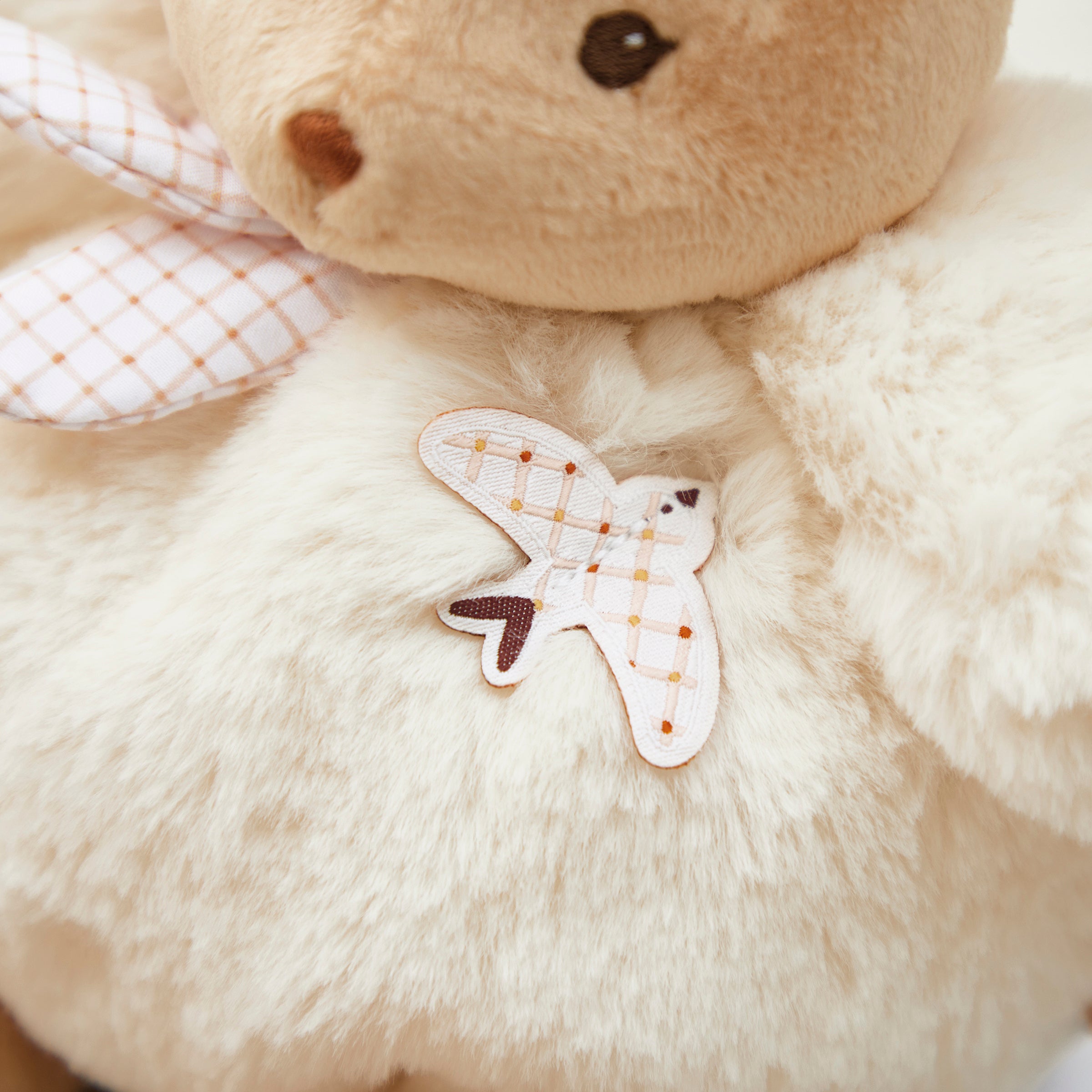 Close-up of a beige teddy bear with a butterfly patch on its chest.