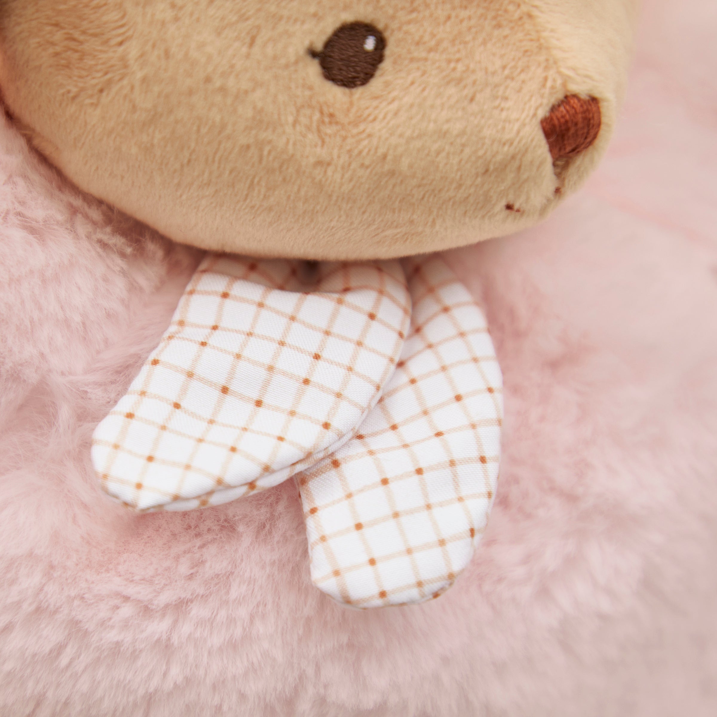 Close-up of a plush teddy bear with checkered paw on a soft pink background