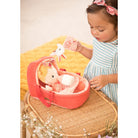 Child playing with a pink toy crib and plush toy on a yellow blanket