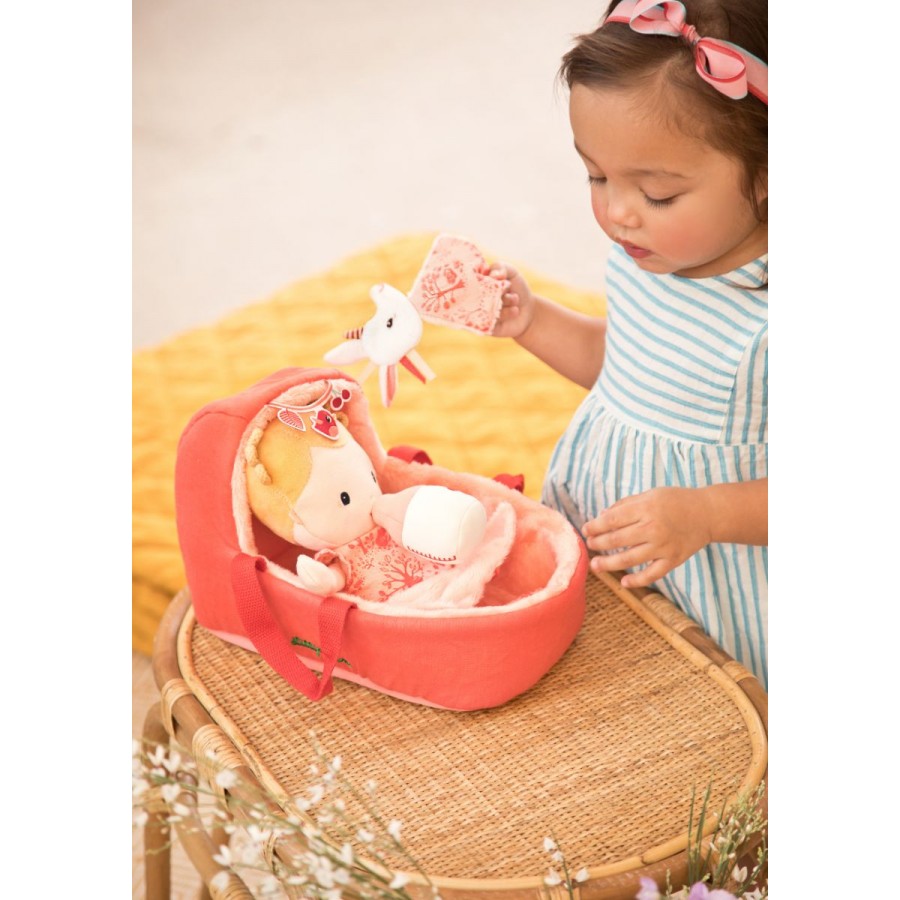 Child playing with a pink toy crib and plush toy on a yellow blanket