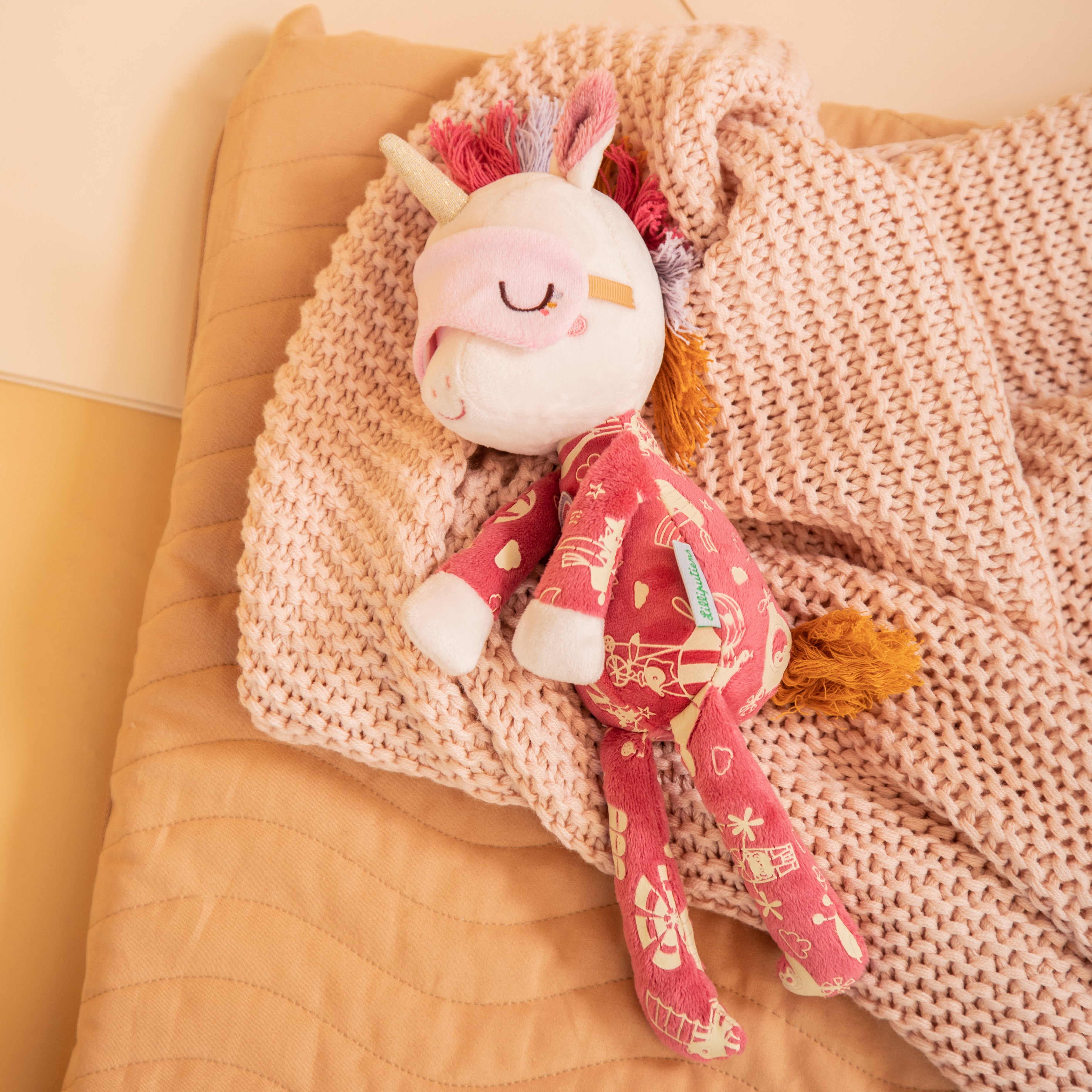 Plush toy unicorn with pink blanket on a beige surface