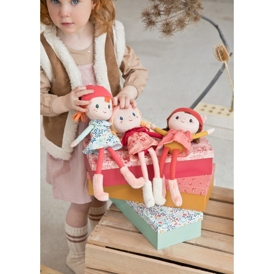 Child holding three dolls with a colorful box on a wooden surface