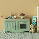 Toy kitchen set with a green stove, wooden counter, and various accessories on a patterned floor.