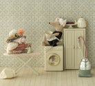 Miniature scene with a toy mouse on a washing machine, teapot, and other items against a patterned wall.