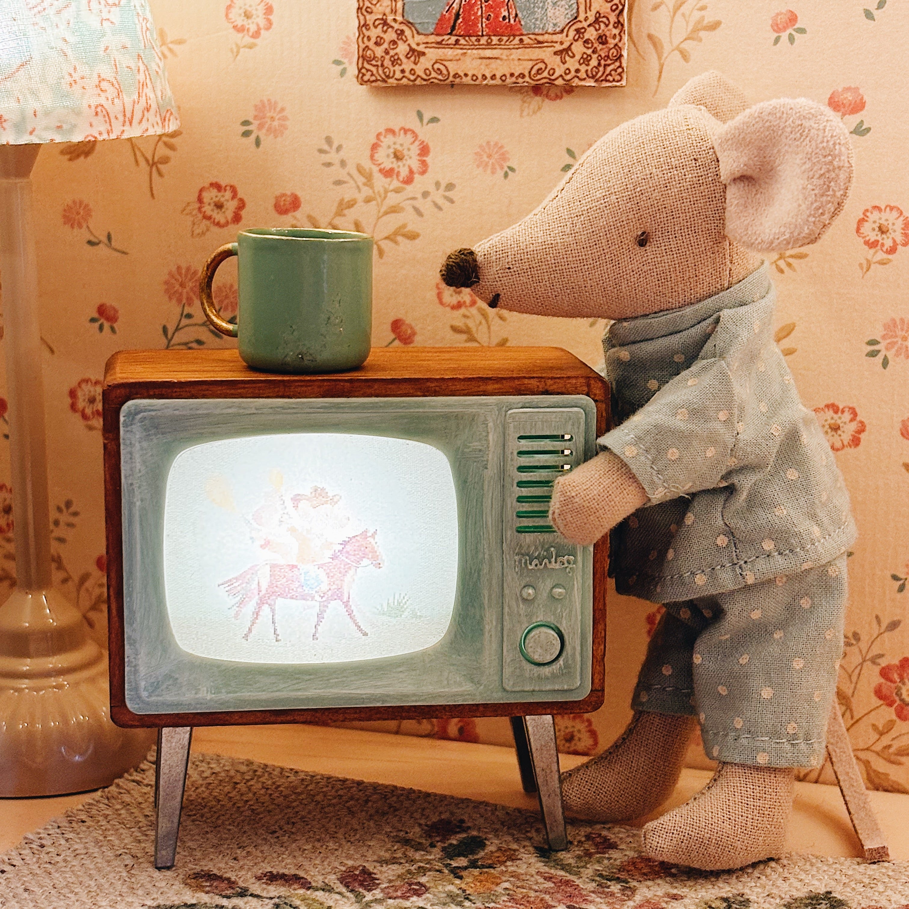 MAileg mouse wearing pyjamas switching on the television in a dolls house living room scene 