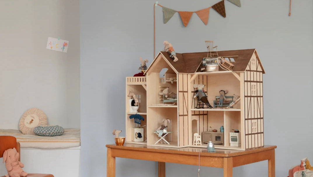 Wooden dollhouse with furniture and accessories on a table against a light gray wall.
