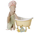 A toy bath scene featuring a beige plush mouse wearing a pink polka-dot shower cap and a green striped towel, sitting beside a cream-colored clawfoot bathtub. A small yellow rubber duck, a blue bottle, and a brush are placed in front on a white background.