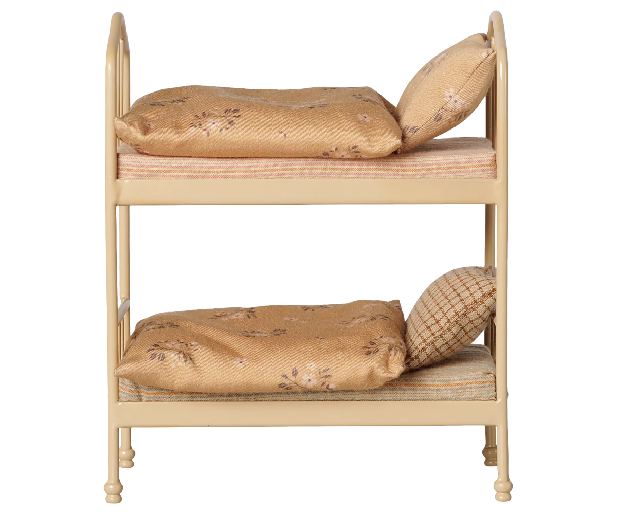 A miniature two-tier dollhouse bed frame in a light beige wood finish, furnished with two tan floral-patterned pillows and striped mattress covers, isolated on a white background.