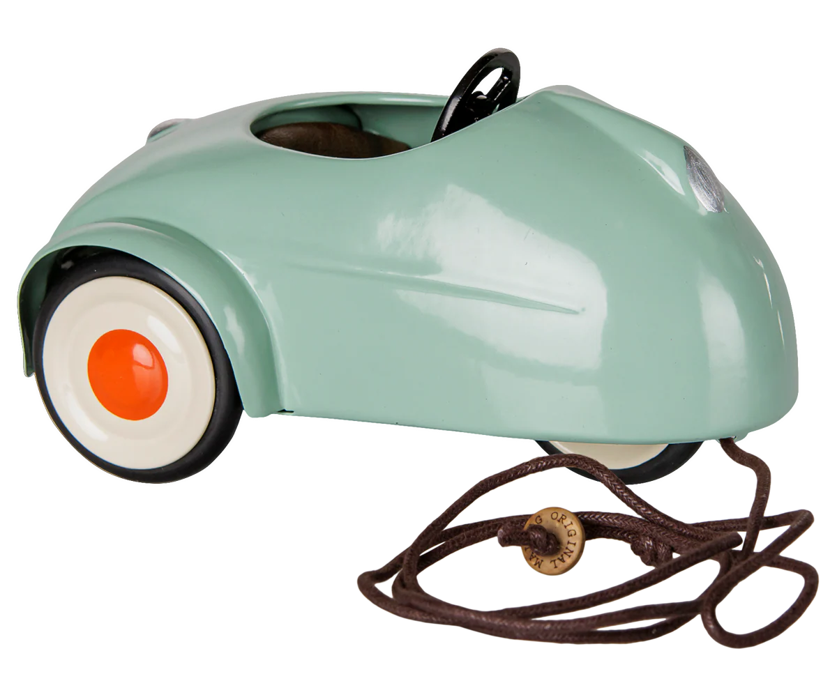 A retro-style pedal toy car in mint green with white wheels, orange centers, a black steering wheel, and a brown pull cord with a wooden knob, shown on a white background.