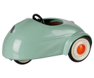 A retro-style pedal toy car in a glossy mint green finish, featuring a black steering wheel, black tires, and white-walled tires with orange center caps, shown on a plain white background.