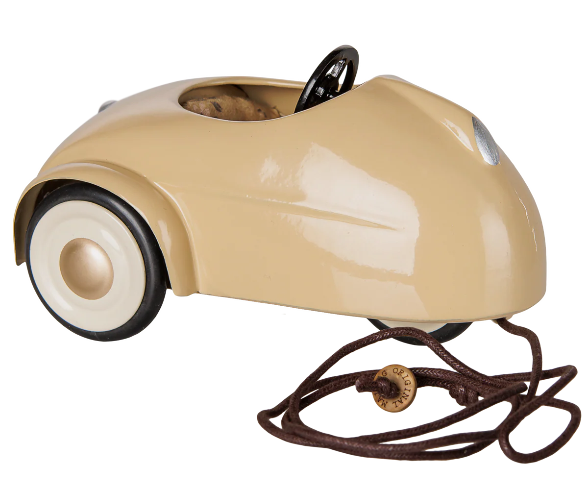 A vintage-style beige pedal car with a glossy finish, featuring a black steering wheel, cream-colored tires, and a brown pull cord with a wooden knob, shown against a plain white background.