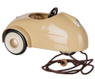 A vintage-style beige pedal car with a glossy finish, featuring a black steering wheel, cream-colored tires, and a brown pull cord with a wooden knob, shown against a plain white background.
