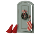 A miniature-style gray arched door decoration with a red-and-white striped stocking hanging from the handle and a matching wreath ornament, shown on a plain white background with two small red boot shapes at the lower left.