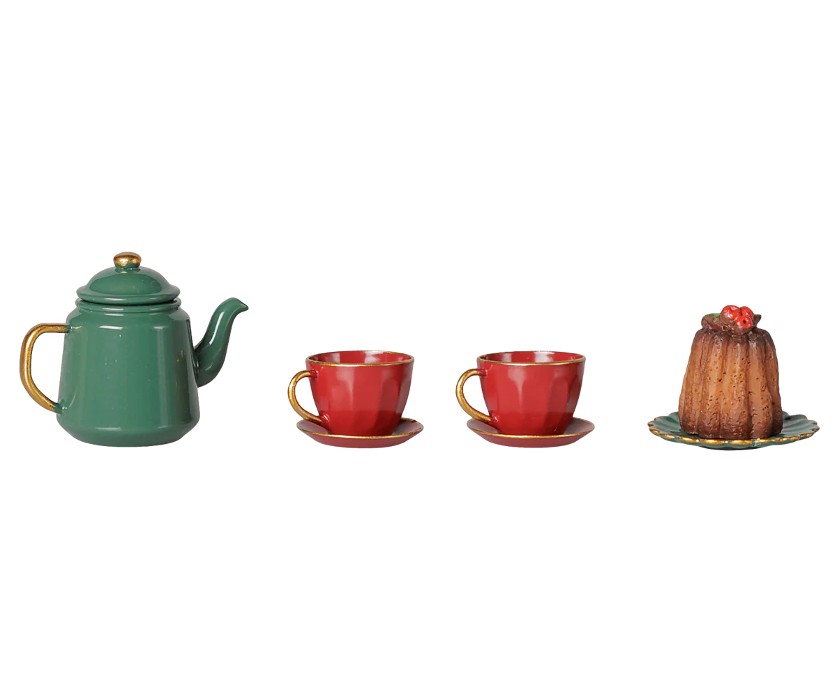 A miniature tea set and dessert display featuring a green teapot with gold accents, two red teacups with saucers, and a small brown pudding on a plate, all arranged on a plain white background.