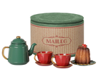 Maileg tea set with a green teapot, two red cups with gold handles, a small cake on a saucer, and a tall round cream-colored tin with a green lid, all on a white background.