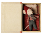 A small plush mouse toy dressed in a red hat and scarf with gray pants, presented inside an open beige gift box with a red patterned cushion.