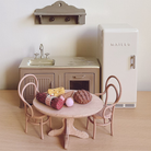 Miniature kitchen set with table, chairs, and refrigerator on a wooden floor.