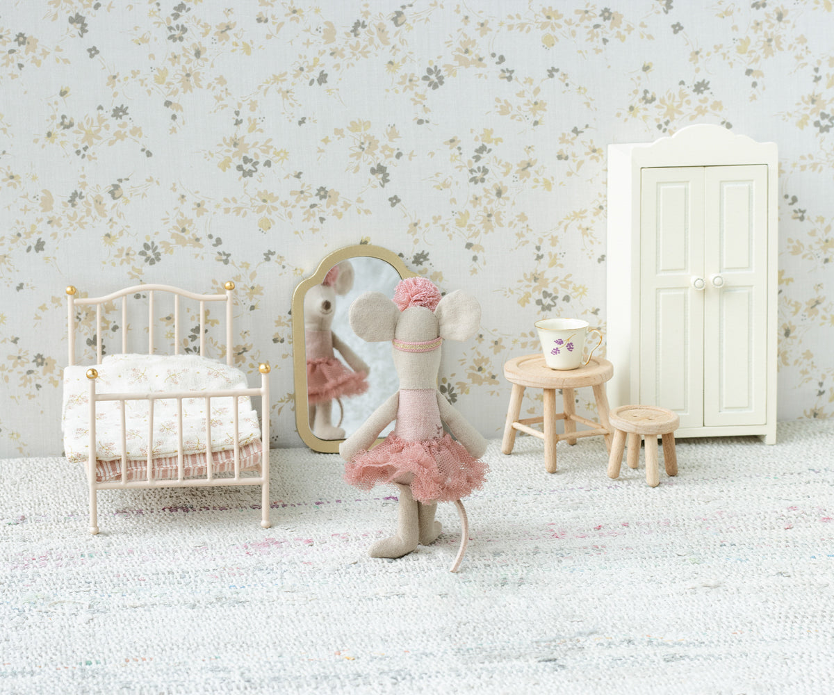 Miniature dollhouse scene with a bed, mirror, and furniture against a floral wallpapered wall.