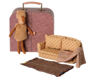 A dollhouse miniature set featuring a patterned suitcase, a small sofa with a throw blanket, and a striped rug, alongside a plush toy sheep.