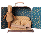 A miniature doll playset inside an open vintage-style suitcase, featuring a plush tan doll, a tiny patterned sofa, a knitted blanket, and a small rug on a white background.